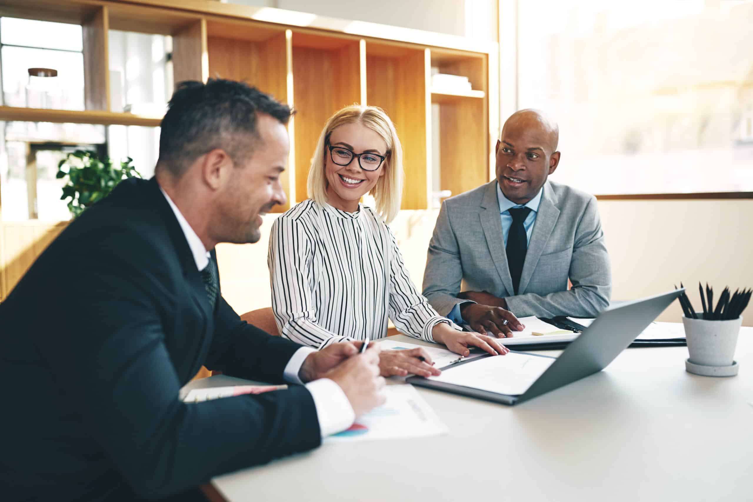 Three smiling businesspeople discussing paperwork together in an